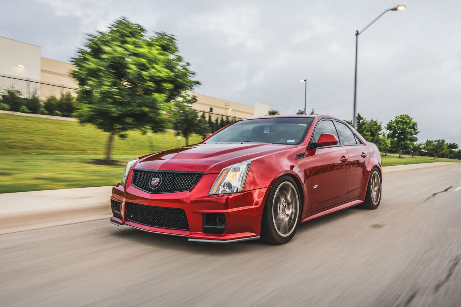 Candy red Cadillac CTS-V with aftermarket wheels photographed in dynamic rolling shot.