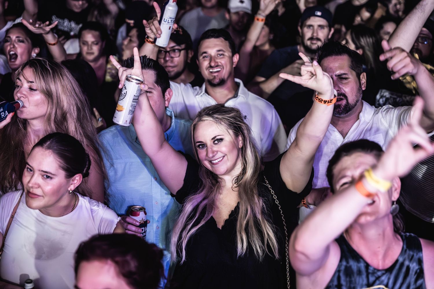 Enthusiastic concert crowd with raised hands dancing and cheering at a music event.