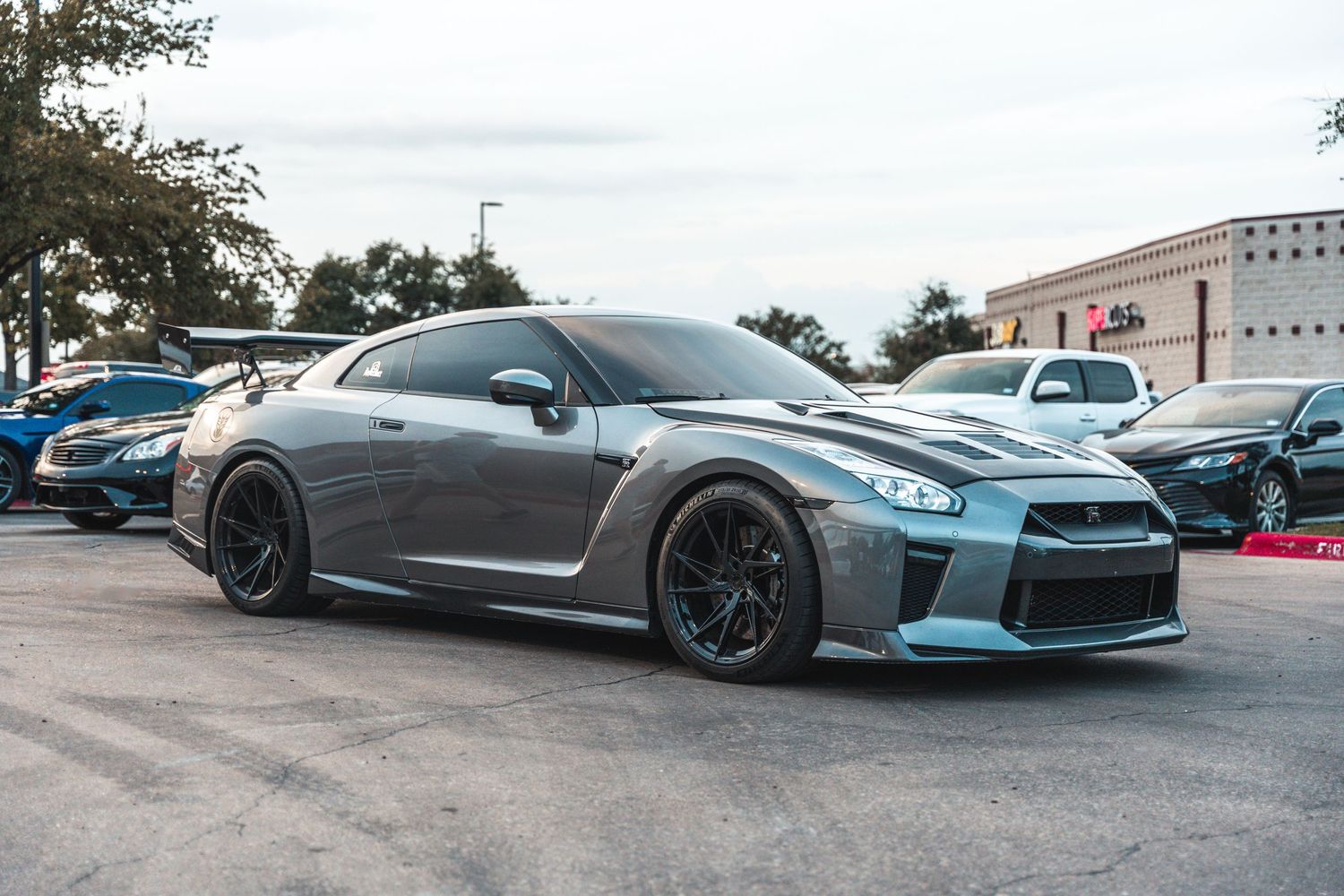 Gray Nissan GT-R with black wheels and aggressive bodywork parked in a commercial lot.