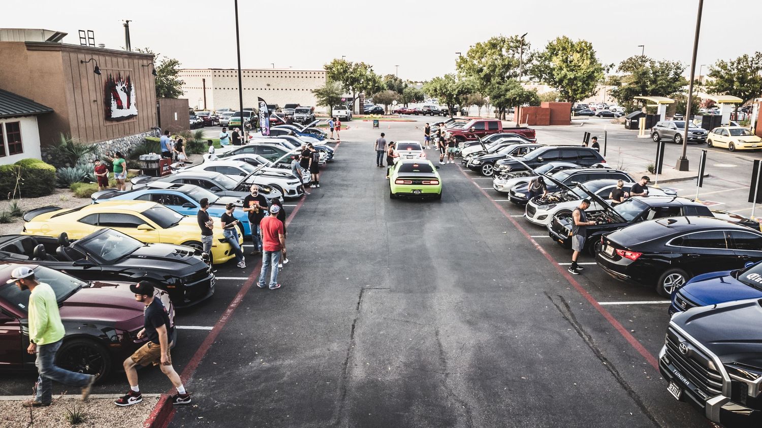 Cars lined up at an outdoor automotive gathering with spectators walking through the parking area.