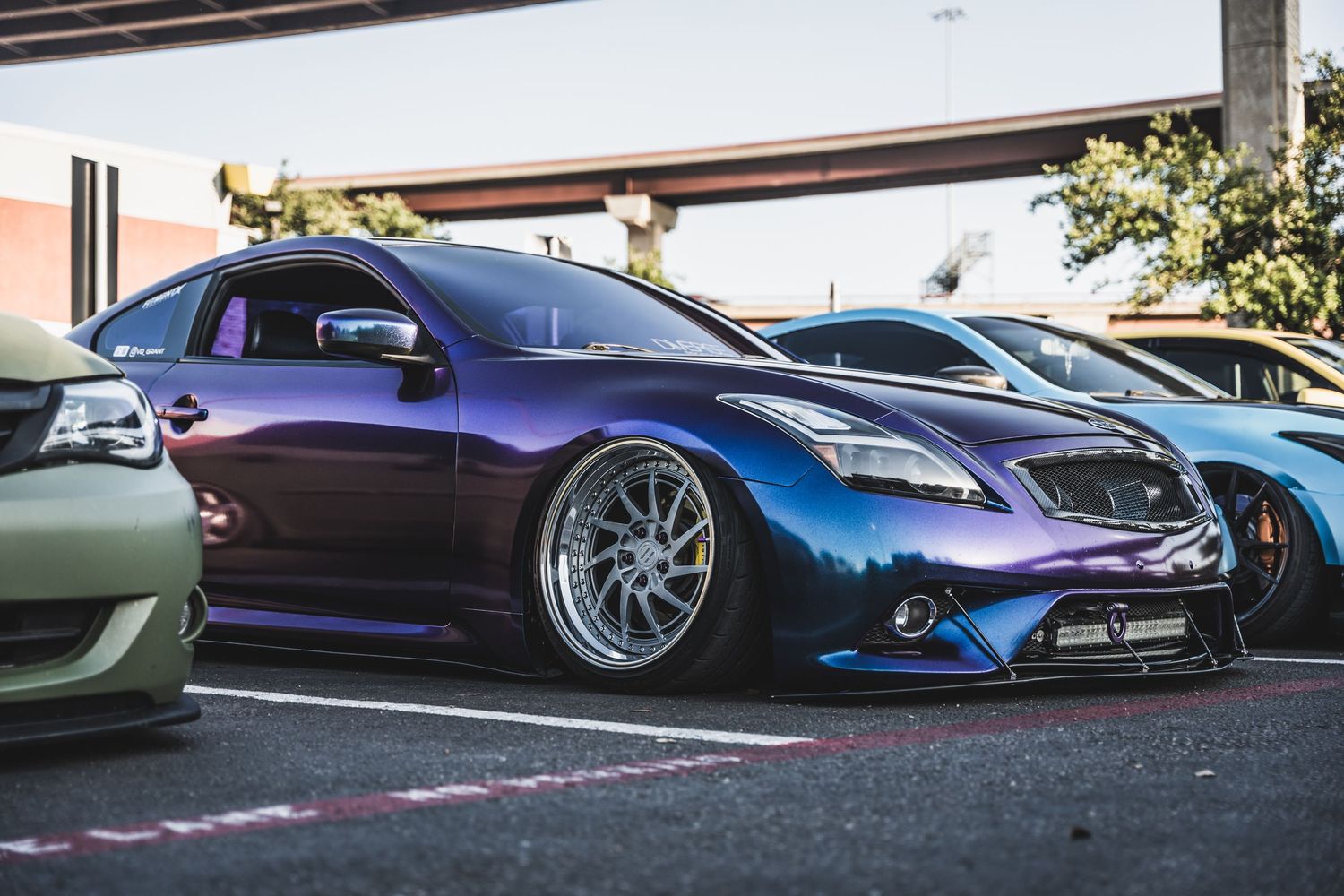 Low-angle view of a custom purple Infiniti with aftermarket wheels and body modifications.