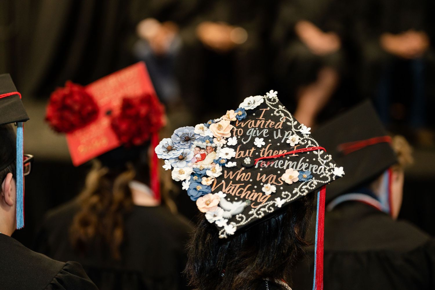 A decorated graduation cap with silver sequins and cursive text at a graduation ceremony.