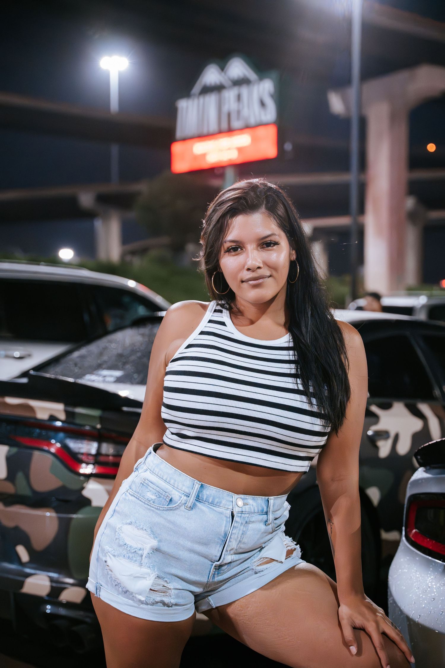 Nighttime photo in front of a store sign showing person in striped crop top and denim shorts.