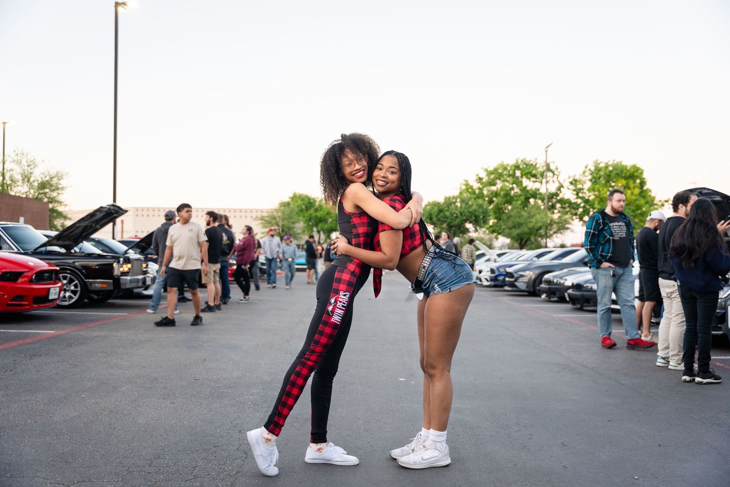 Two friends sharing a joyful moment together in a parking lot with cars in the background.