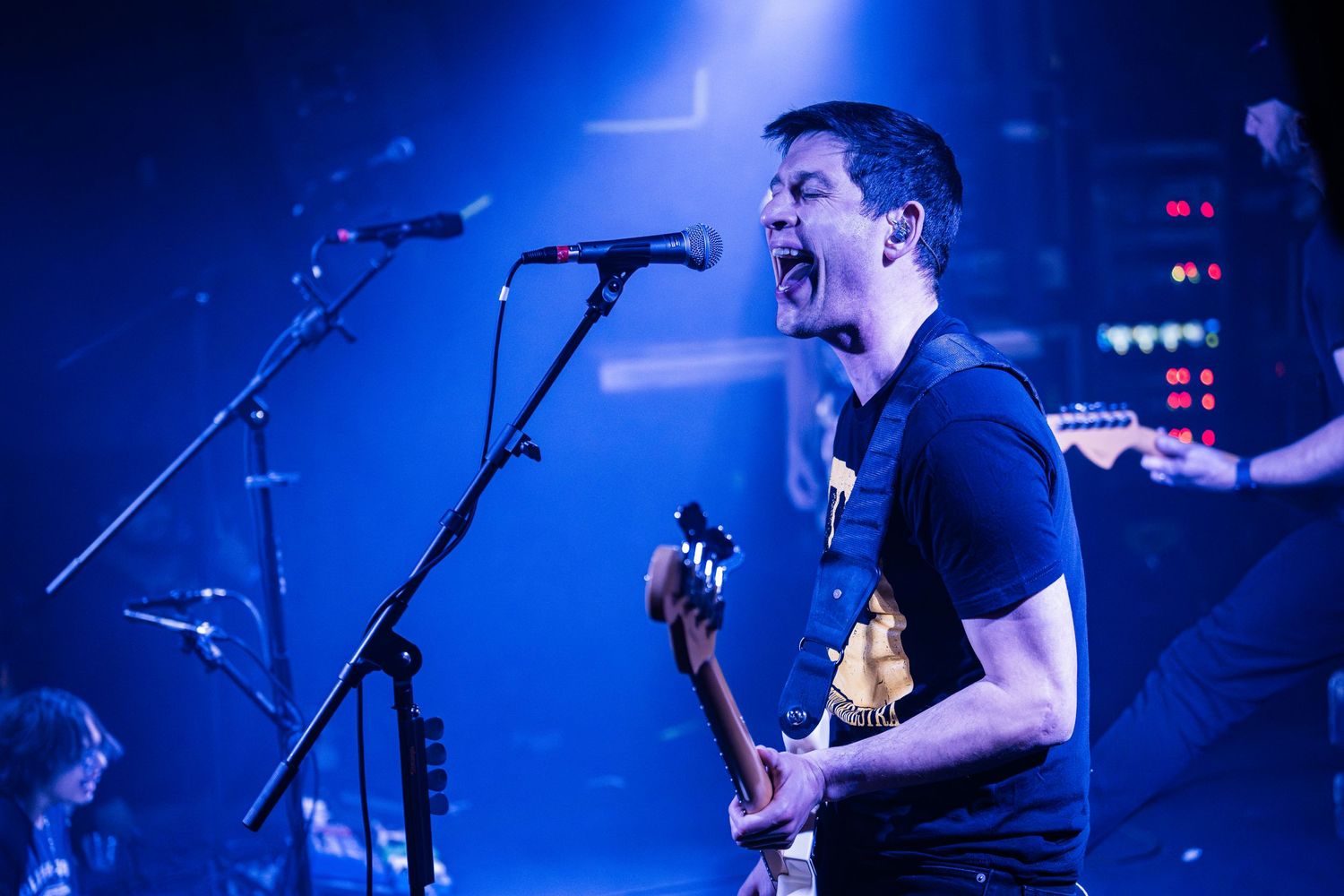 Passionate musician playing guitar and singing during an intense performance under blue stage lights.