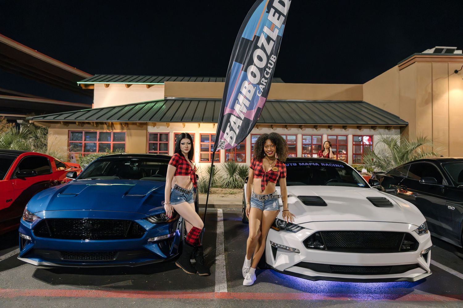 Two blue and white Ford Mustangs on display at a car show with promotional banner.