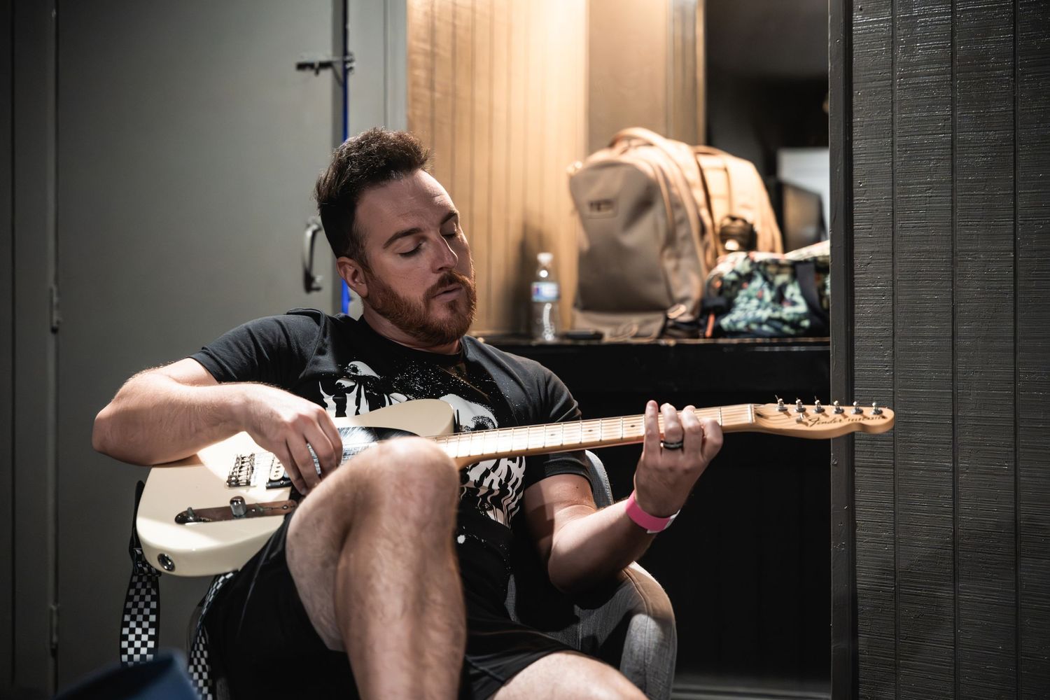 Musician practices guitar while sitting in a casual backstage setting.