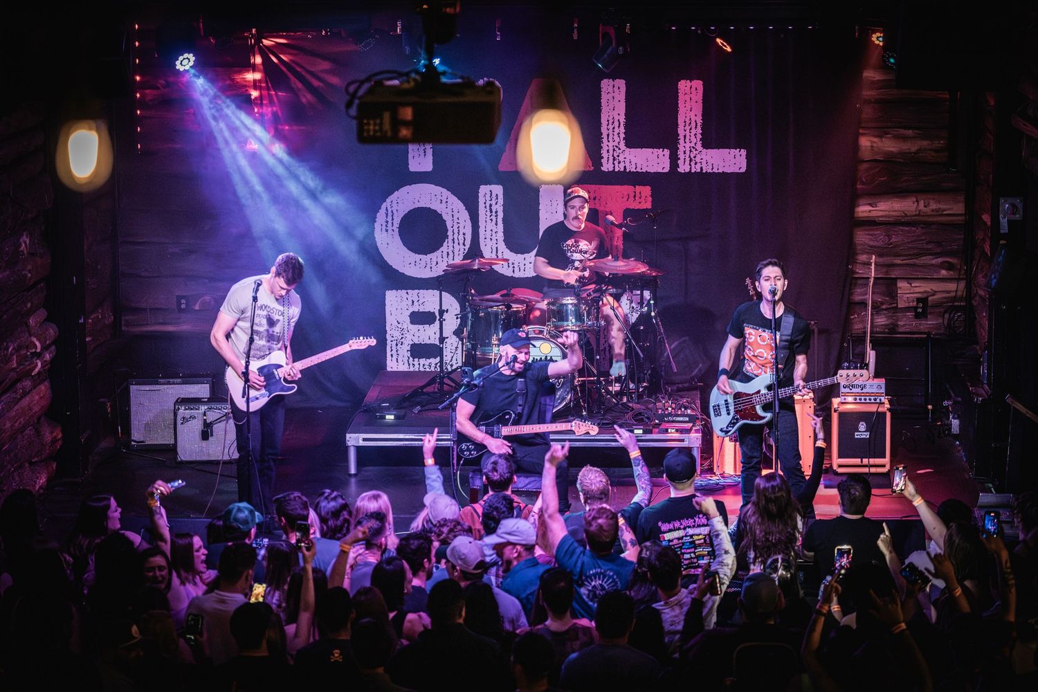 Rock band performing live on stage with illuminated 'ALL OUT' sign and energetic crowd.