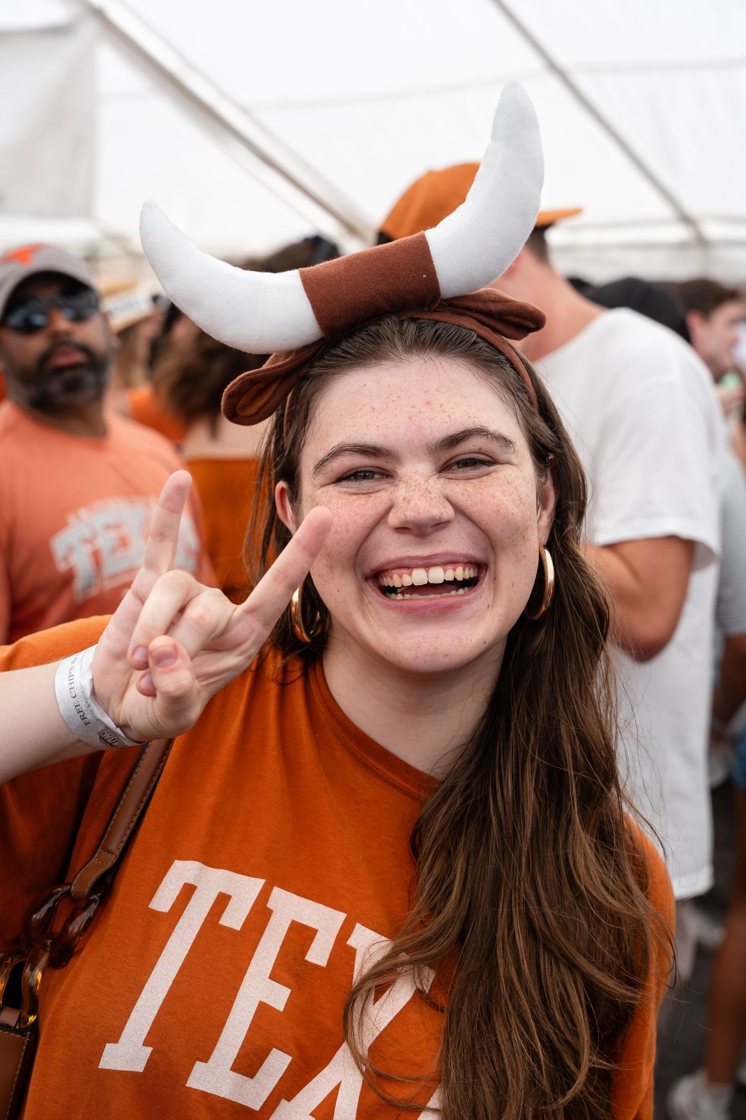 Festival attendee in orange Texas shirt wearing longhorn horns makes peace sign.
