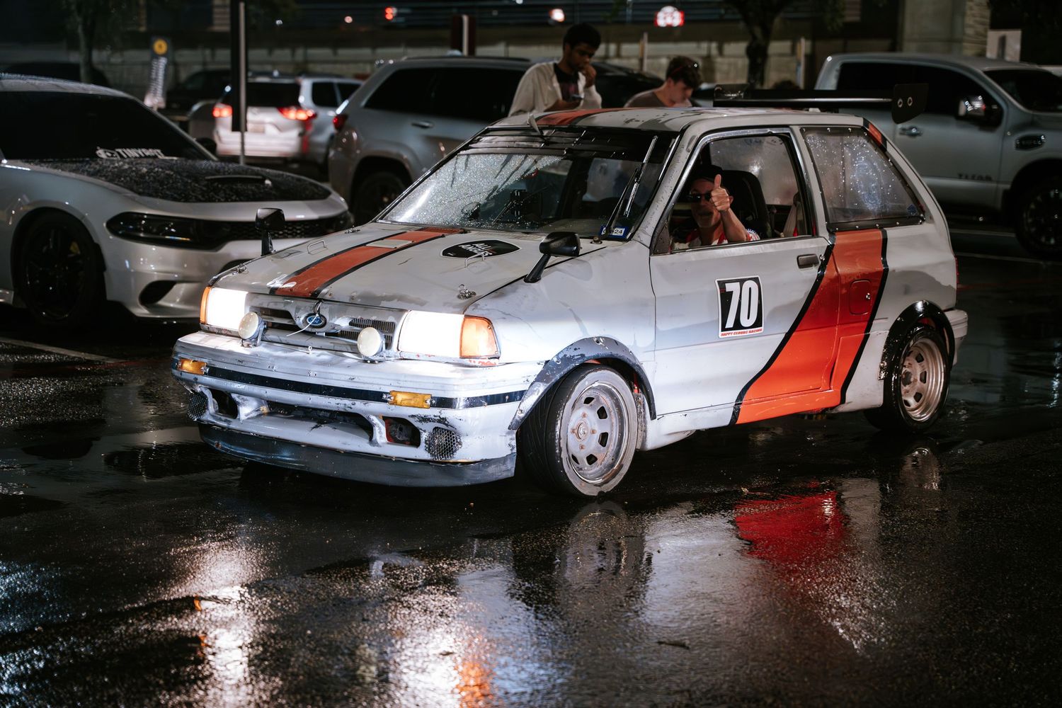 Classic white Ford Fiesta rally car with racing livery parked in a wet lot at night.