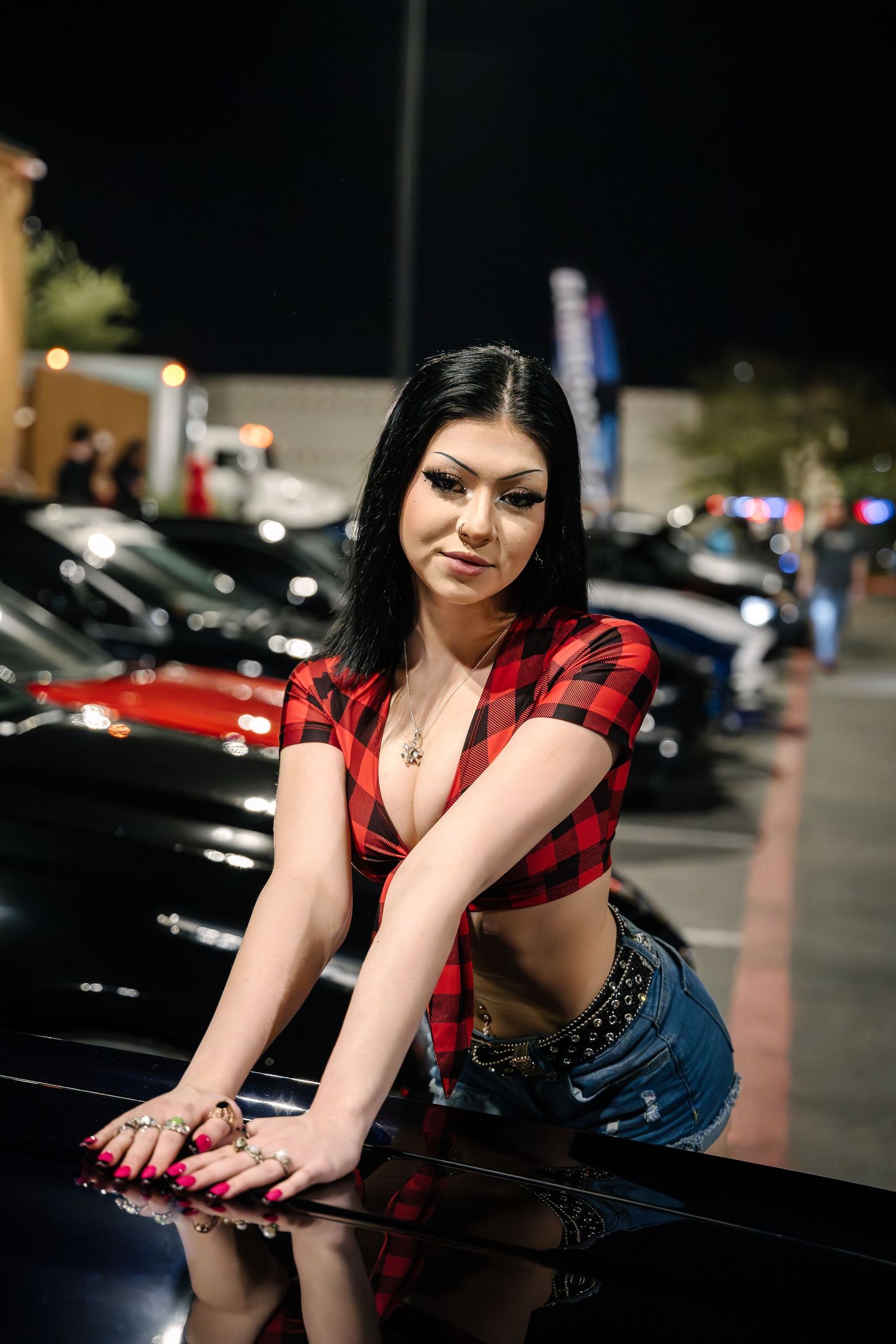 A red plaid cropped shirt and denim shorts outfit styled against a black car at night in a parking lot.