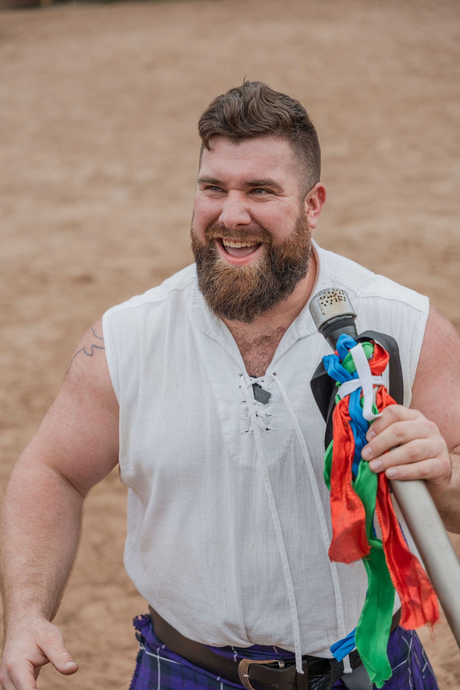Bearded performer in white renaissance shirt holding colorful ribbons at outdoor festival.