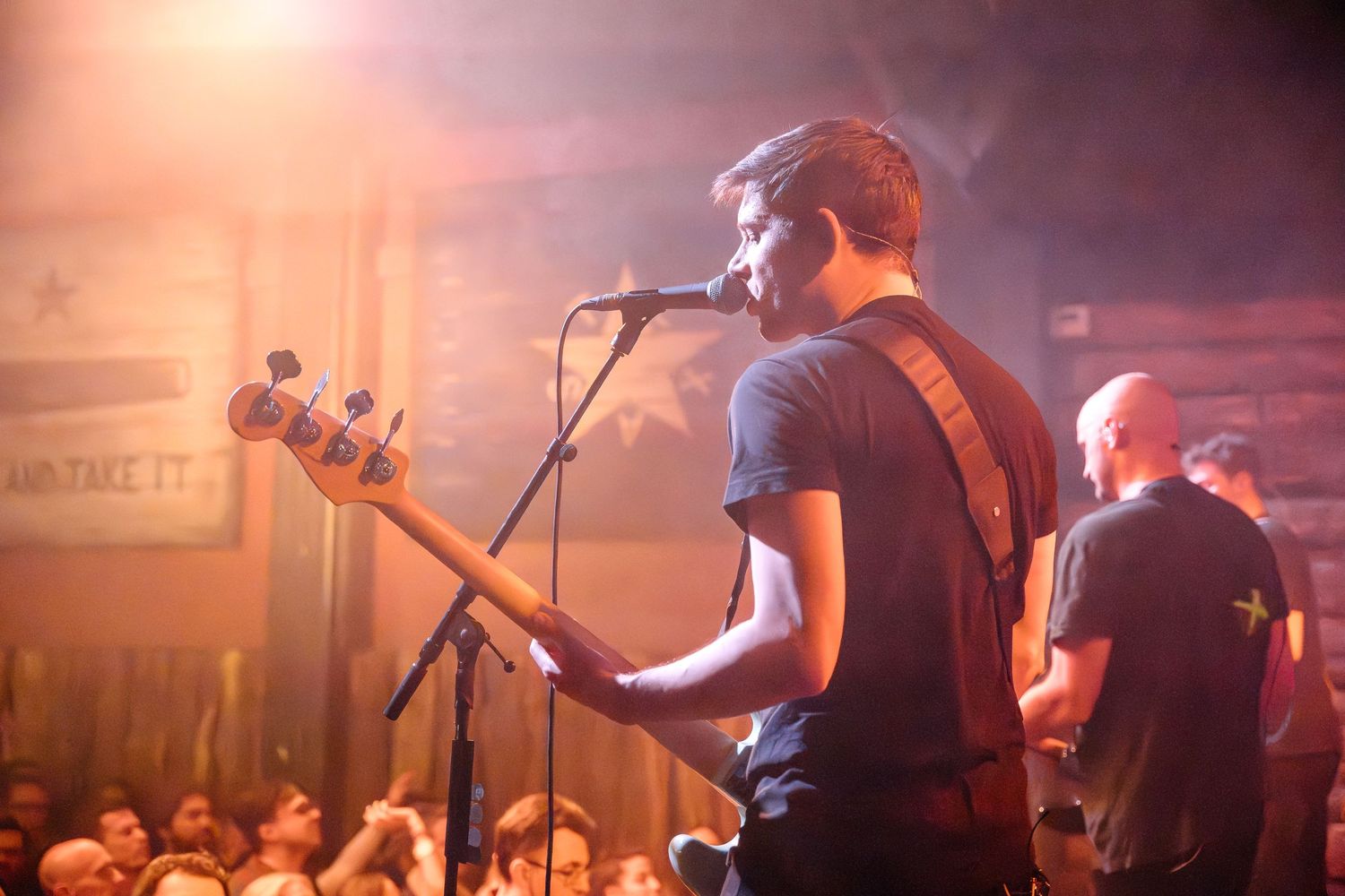 Musician playing bass guitar on stage during live performance with atmospheric lighting.