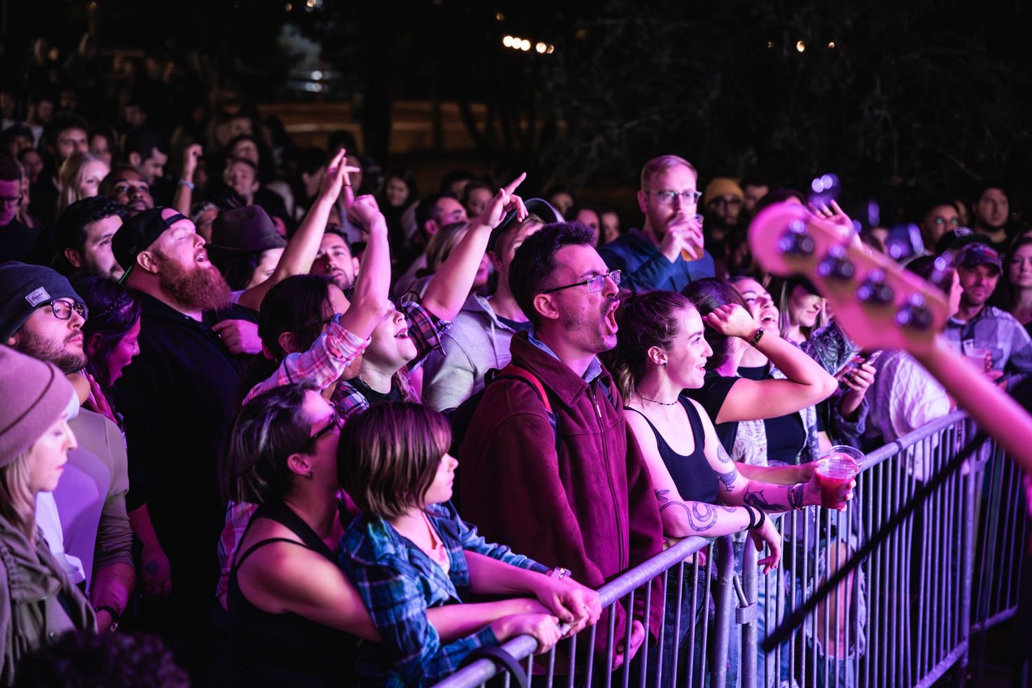 Enthusiastic concert crowd at a music venue with hands raised under purple lighting.