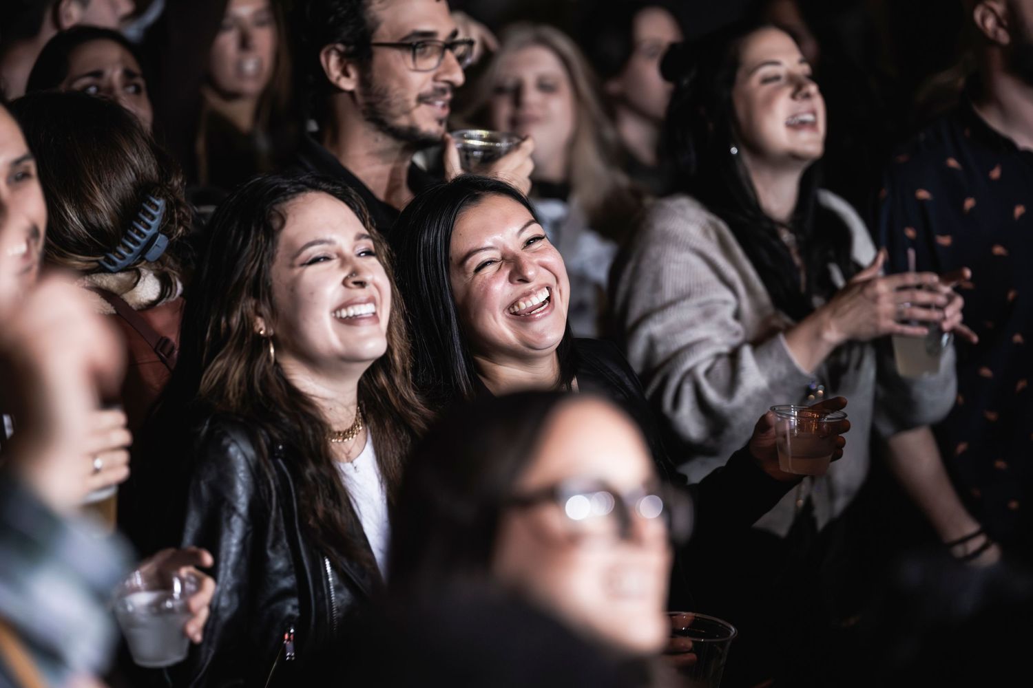 Concert audience members smiling and enjoying live music performance in dark venue.