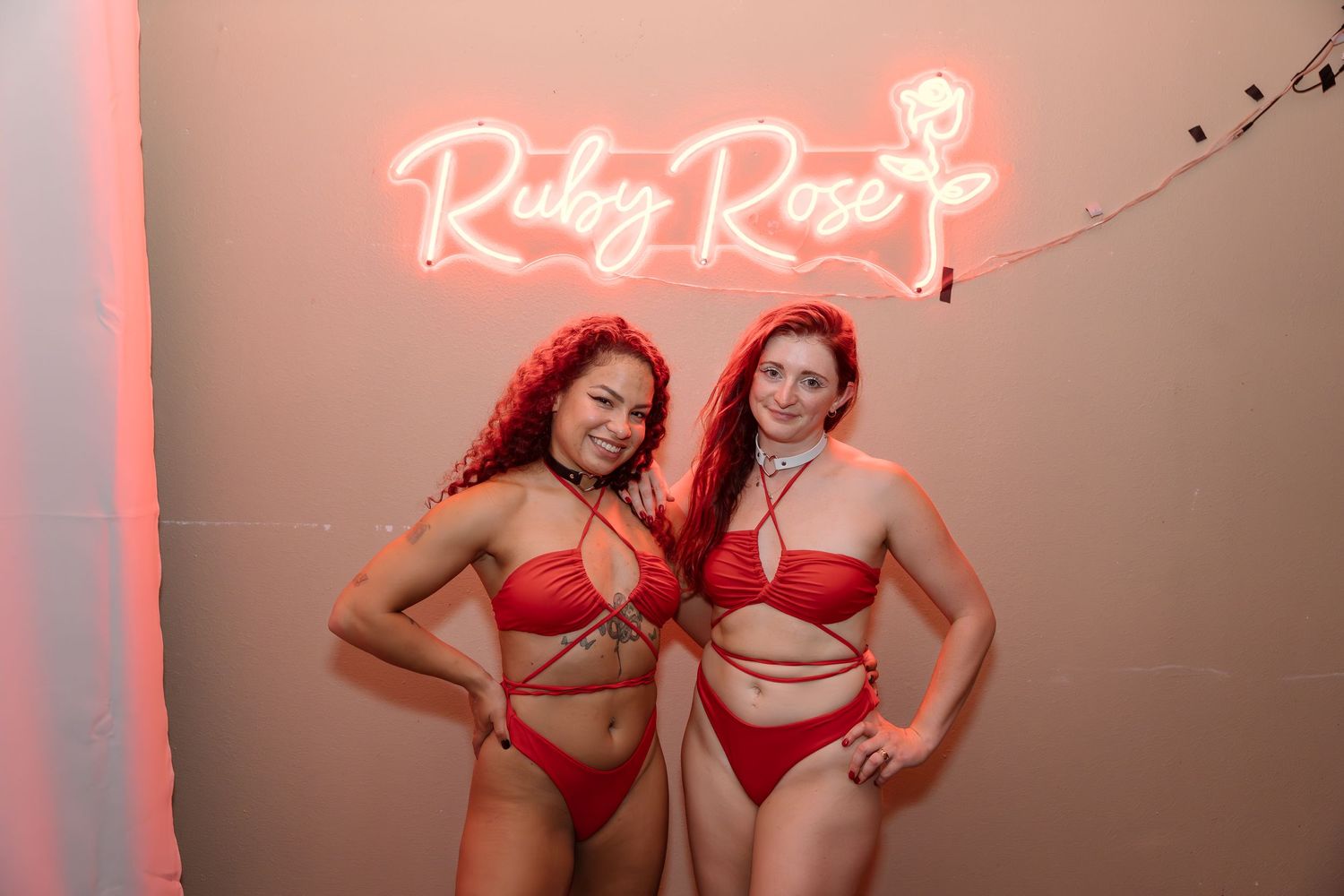 Two people posing under pink neon 'Ruby Rose' sign.