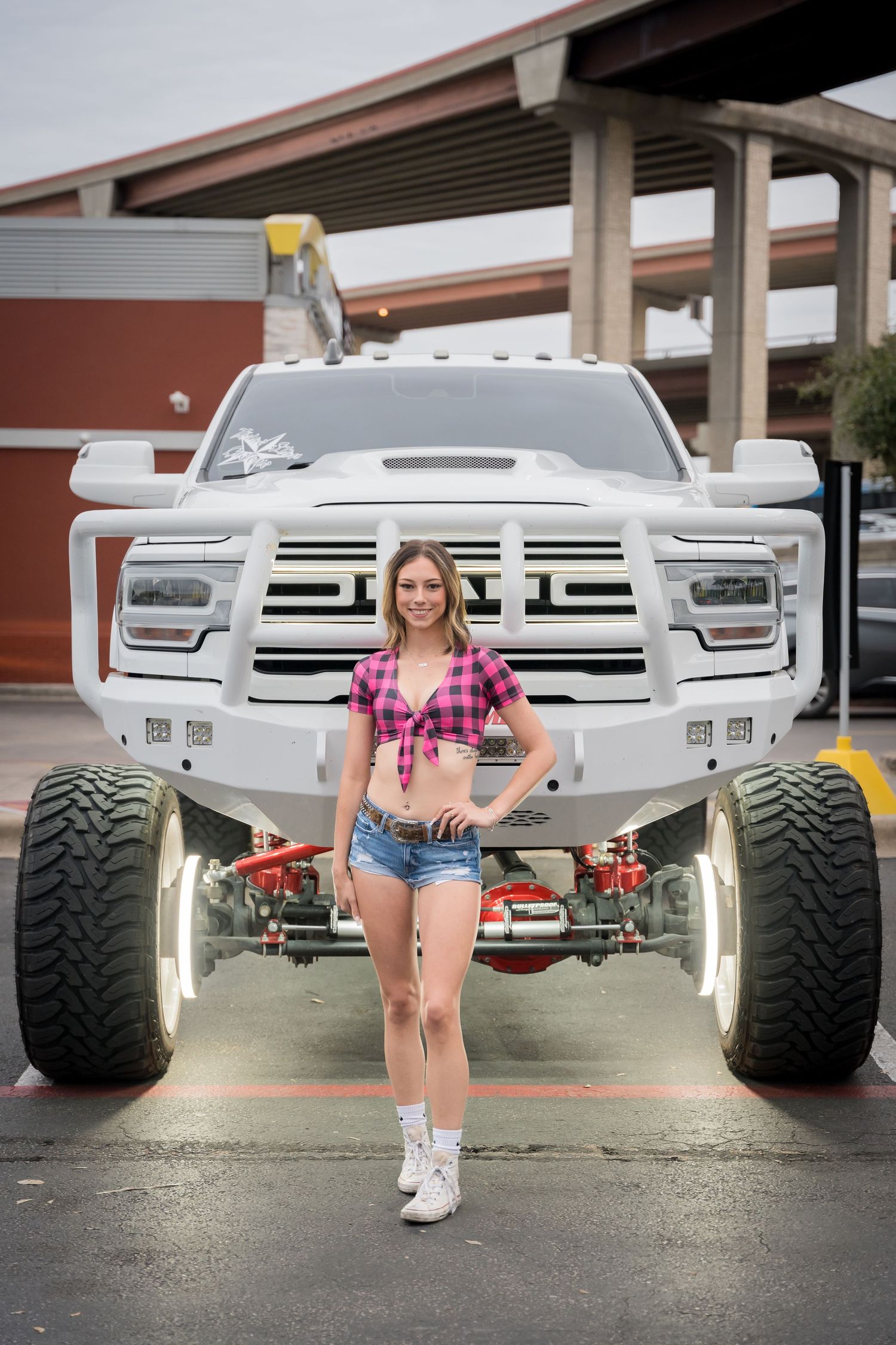 Custom lifted white pickup truck with LED lights and oversized tires parked under covered area.