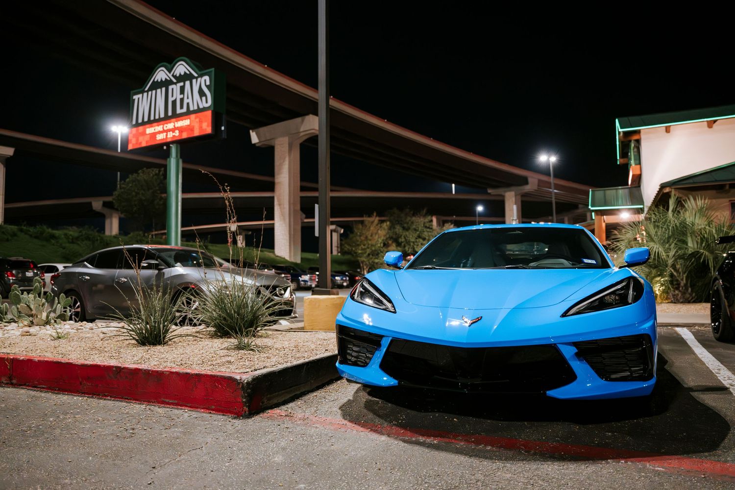 Blue Chevrolet Corvette parked outside a restaurant entrance at night.