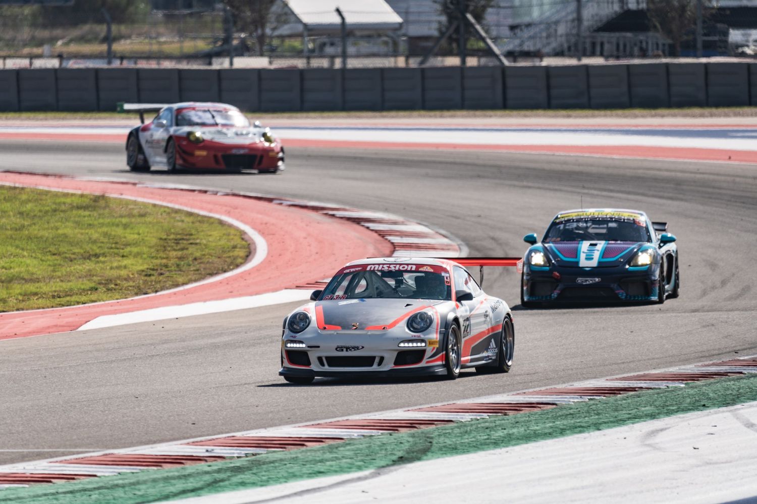 Racing Porsche GT3 leads a pack of cars through a circuit corner.