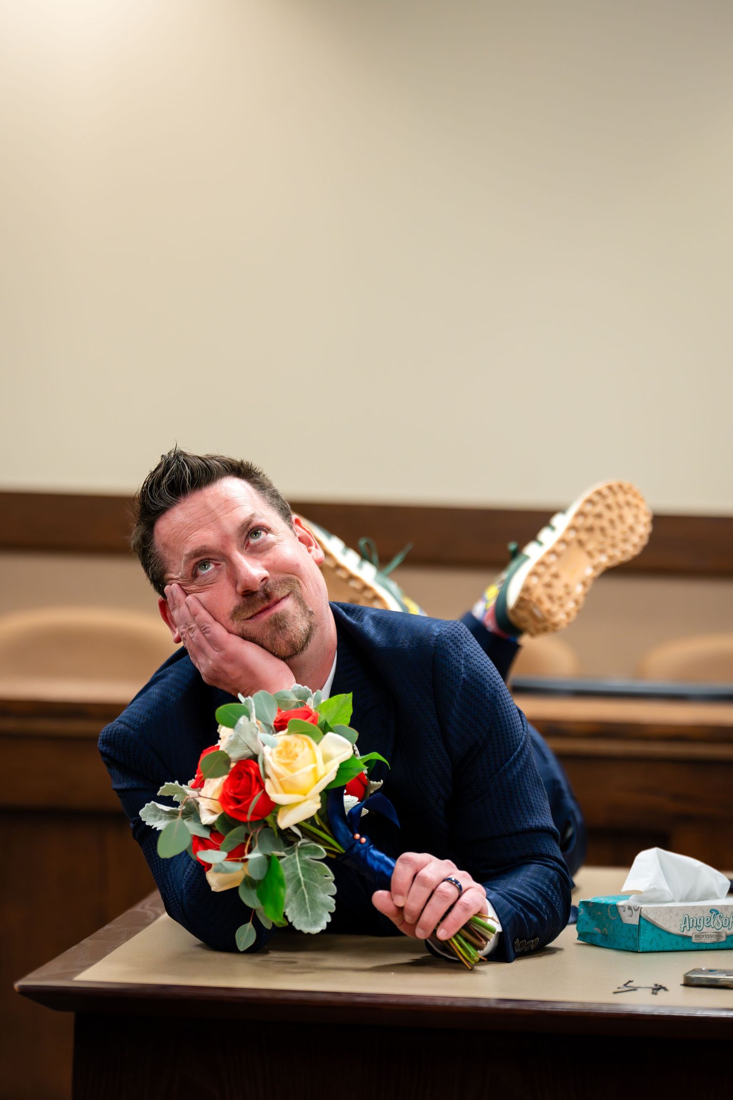 Person in navy suit poses playfully on courthouse desk with flowers.