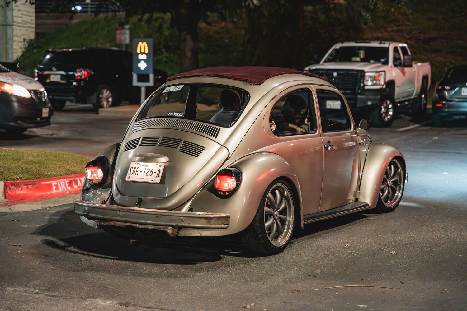 Modified silver Volkswagen Beetle with aftermarket wheels parked at night.