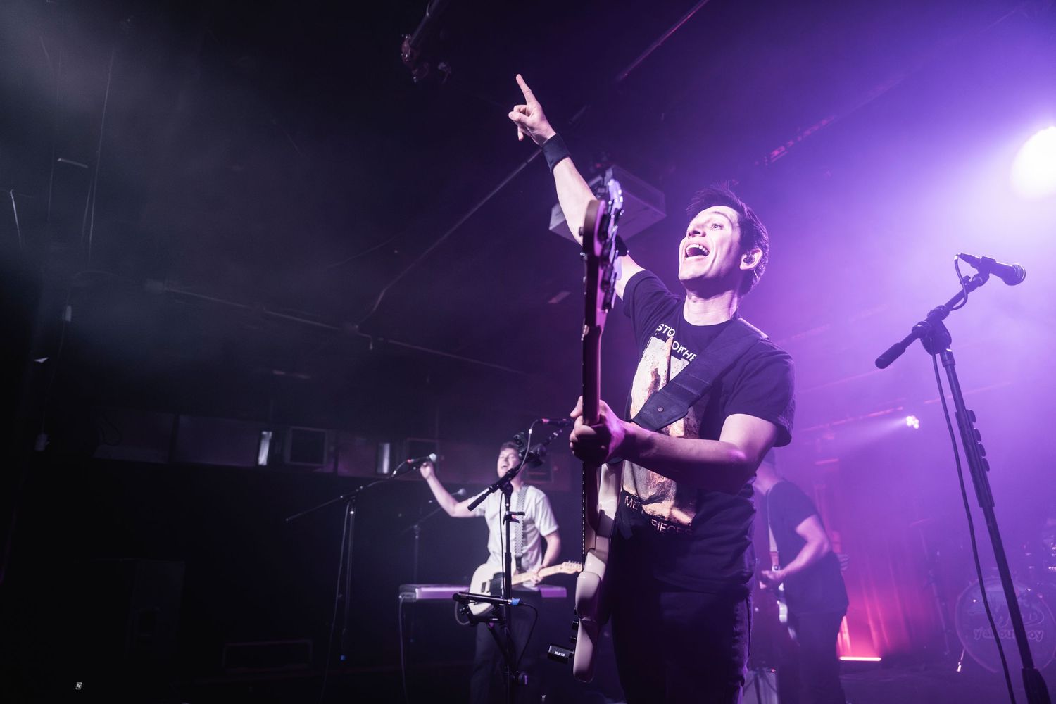 Musicians performing energetically on stage with dramatic purple backlighting.