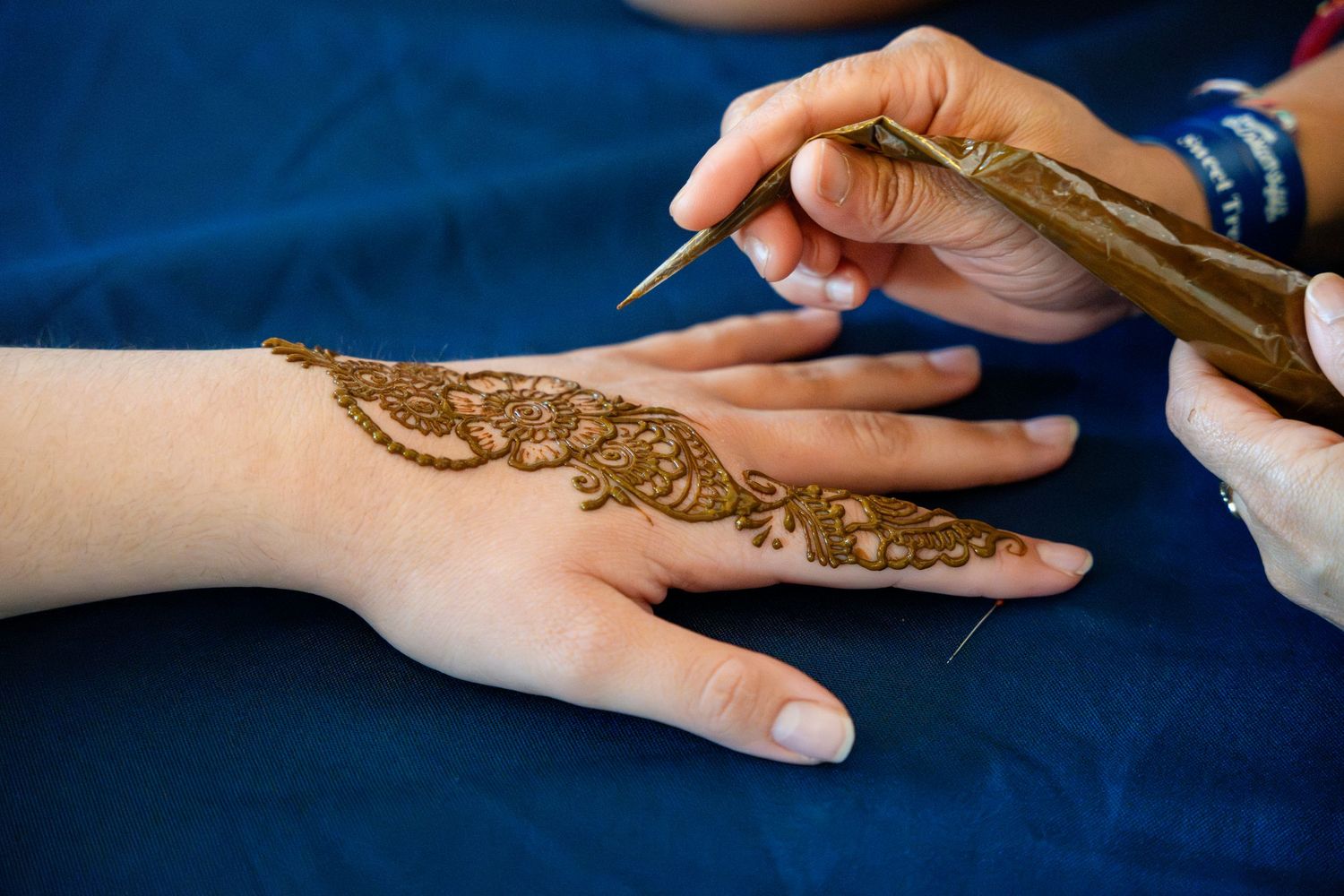 Intricate henna design being applied to a hand with natural dye against a dark blue background.