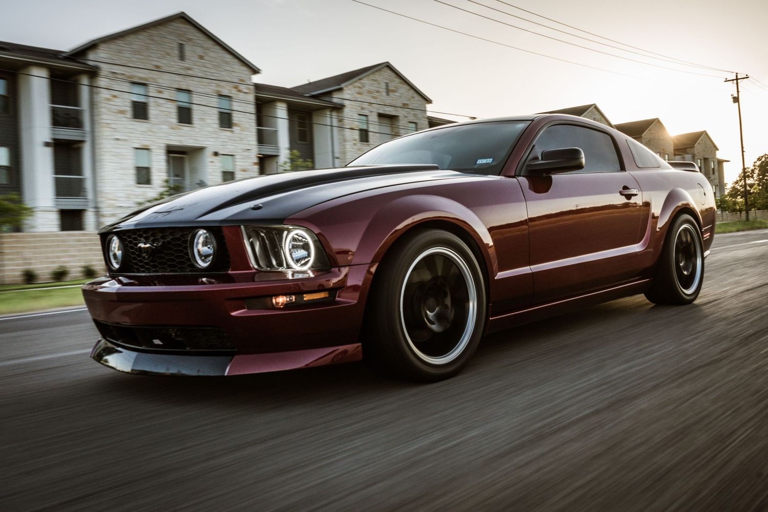 Custom maroon Ford Mustang GT with black wheels photographed in motion on city street.