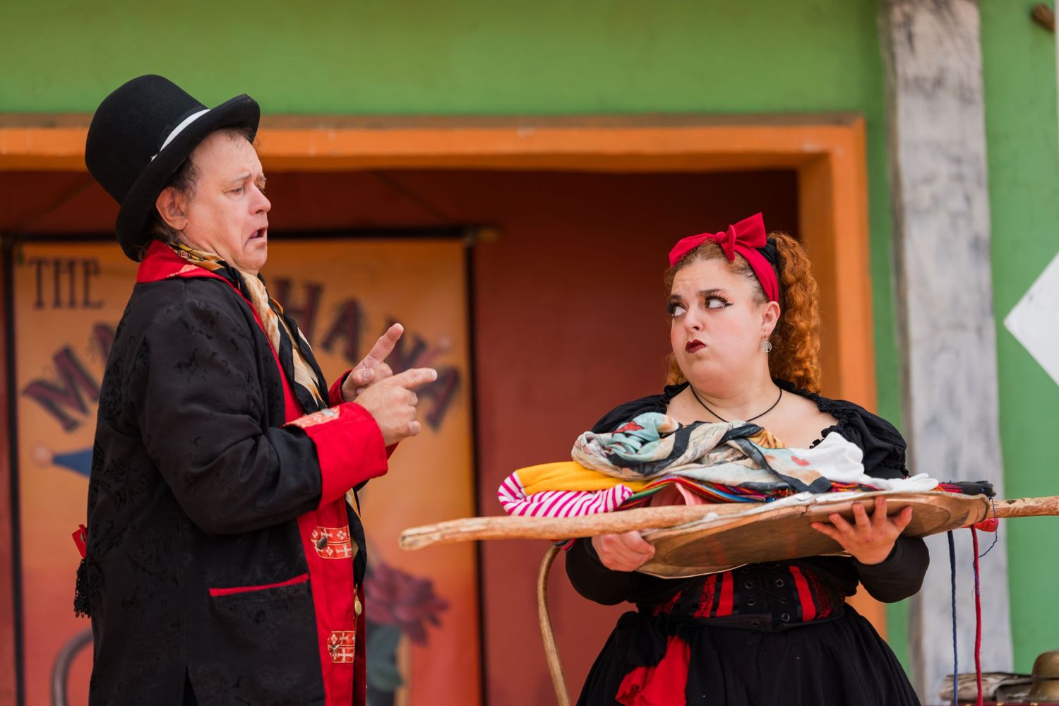 Theatrical performers in period costumes interact during a comedic renaissance fair performance.