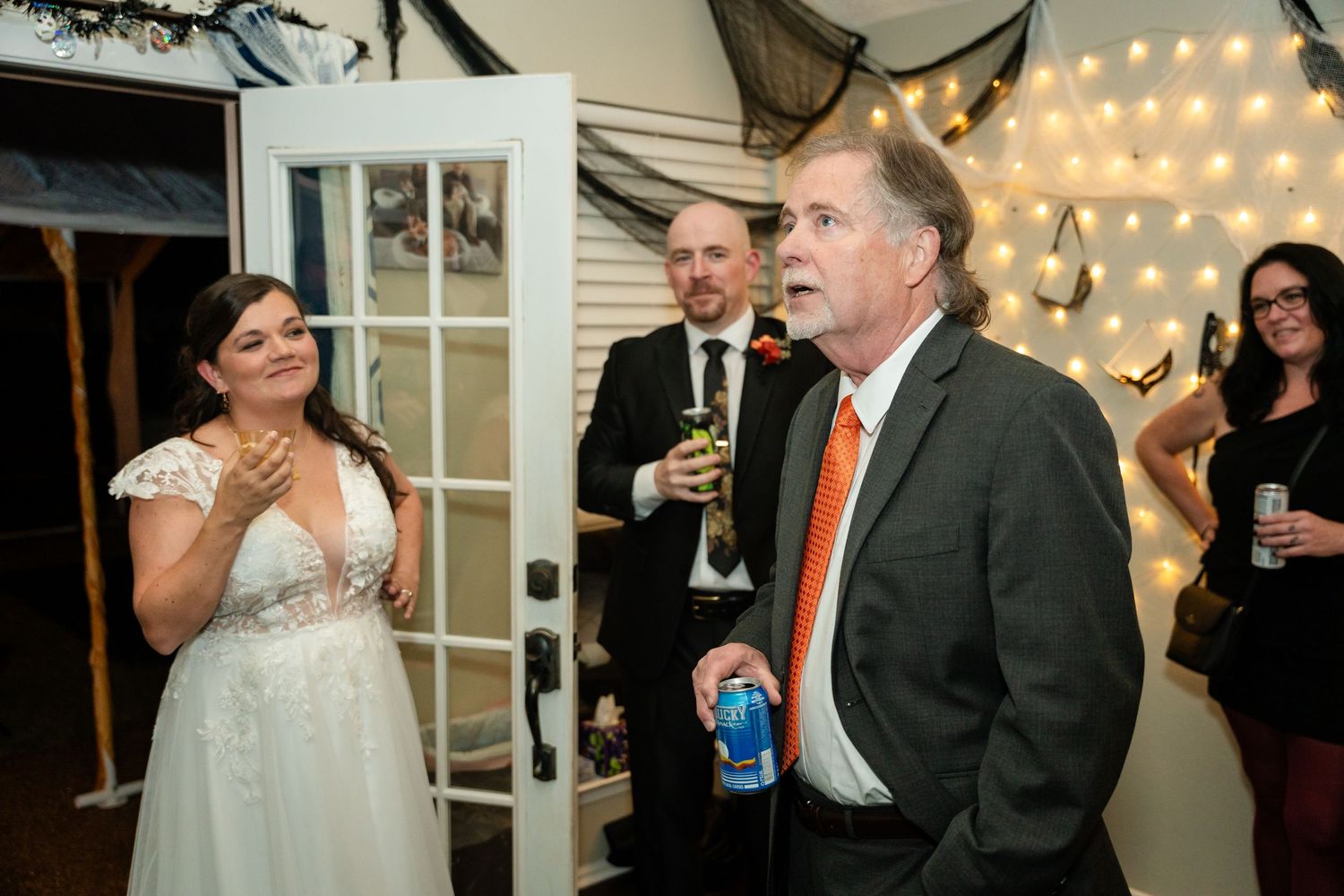 Wedding reception guests share drinks and laughter in a room decorated with string lights.