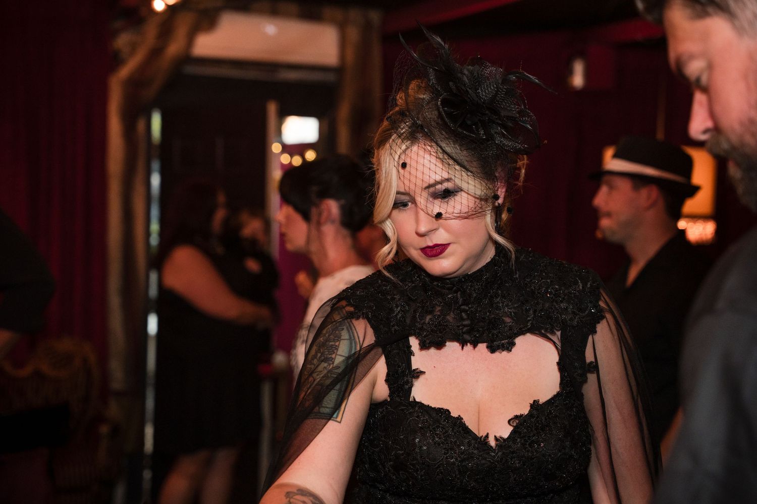 Gothic-themed party scene with elegant black lace and formal attire against red velvet curtains.