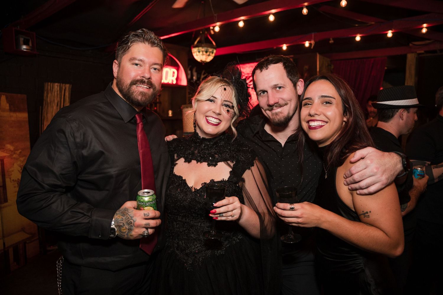 Group of friends celebrating at a bar with red ambient lighting and neon signs.