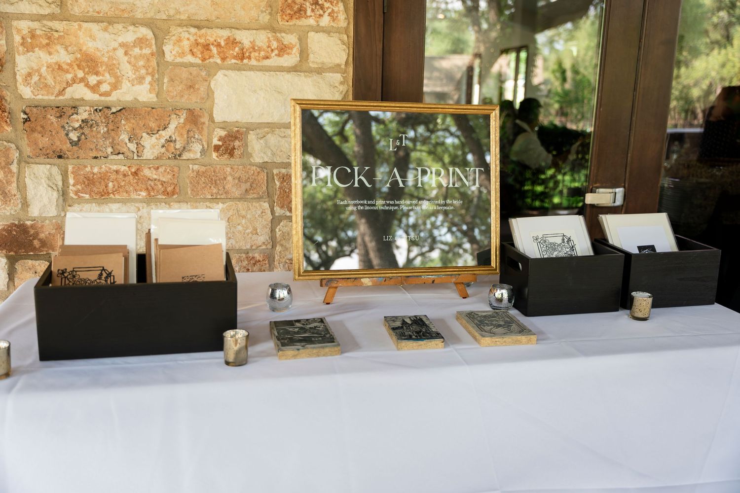 Black and white printed materials on display at a wedding event sign-in table with rustic stone wall backdrop.