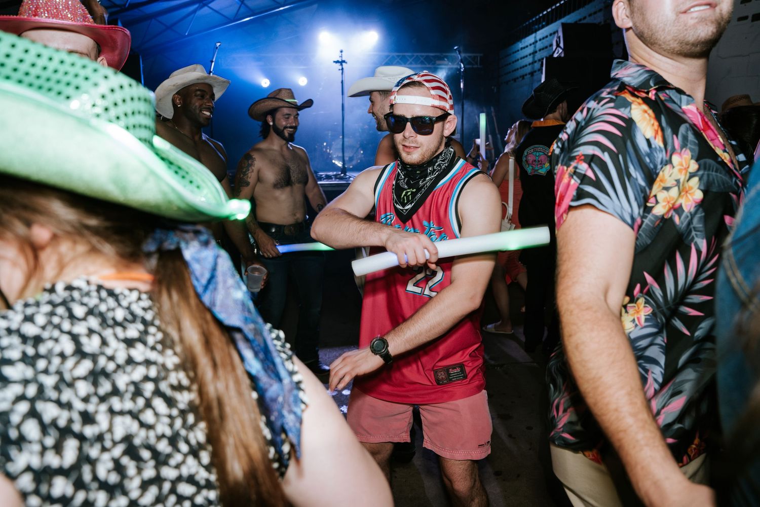 Guests in western attire and colorful clothing dance at a lively party under blue lights.