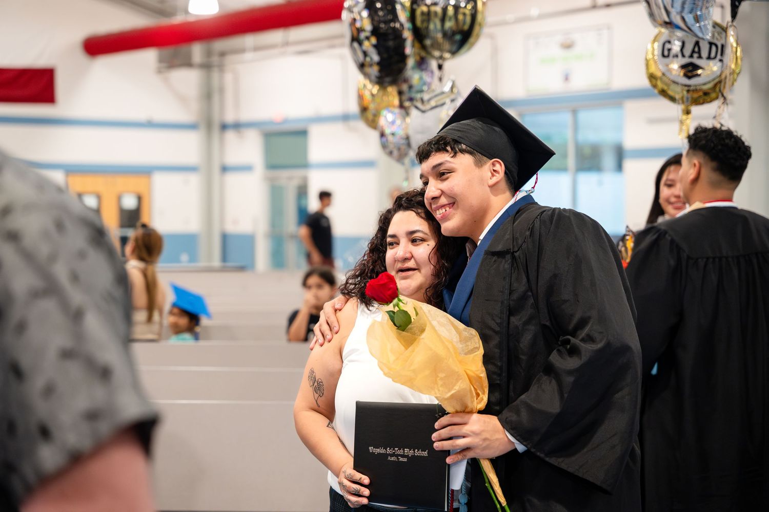 A graduation celebration captured in an indoor venue with celebrants and decorative balloons.