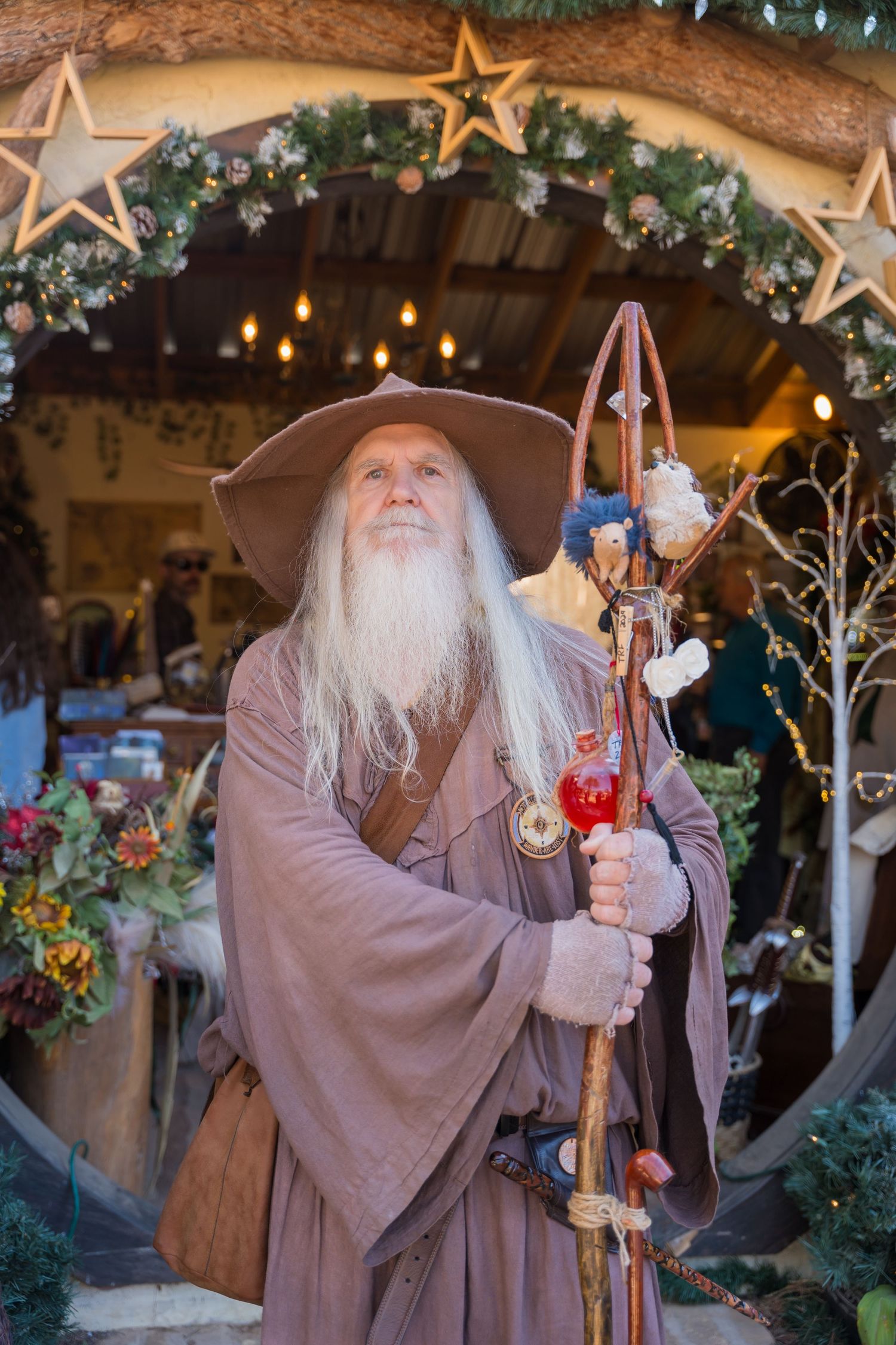 Costumed wizard character with staff poses under decorated archway with stars and greenery.