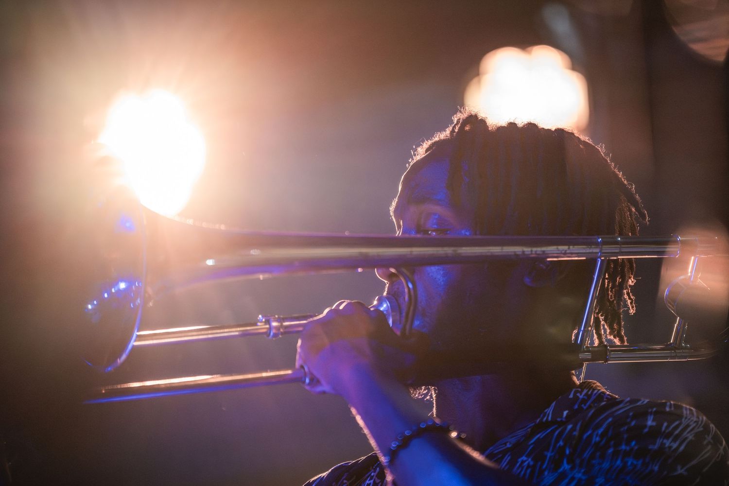 Trombone player performing on stage with dramatic lighting and bokeh effects in the background.