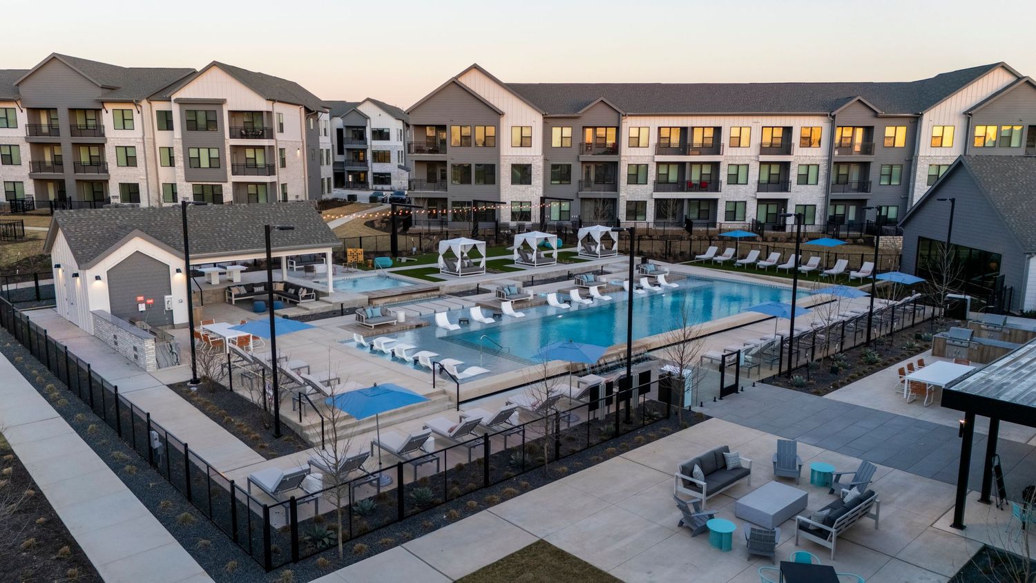 Modern apartment complex with luxurious pool area and outdoor seating during sunset creating a resort-like ambiance.