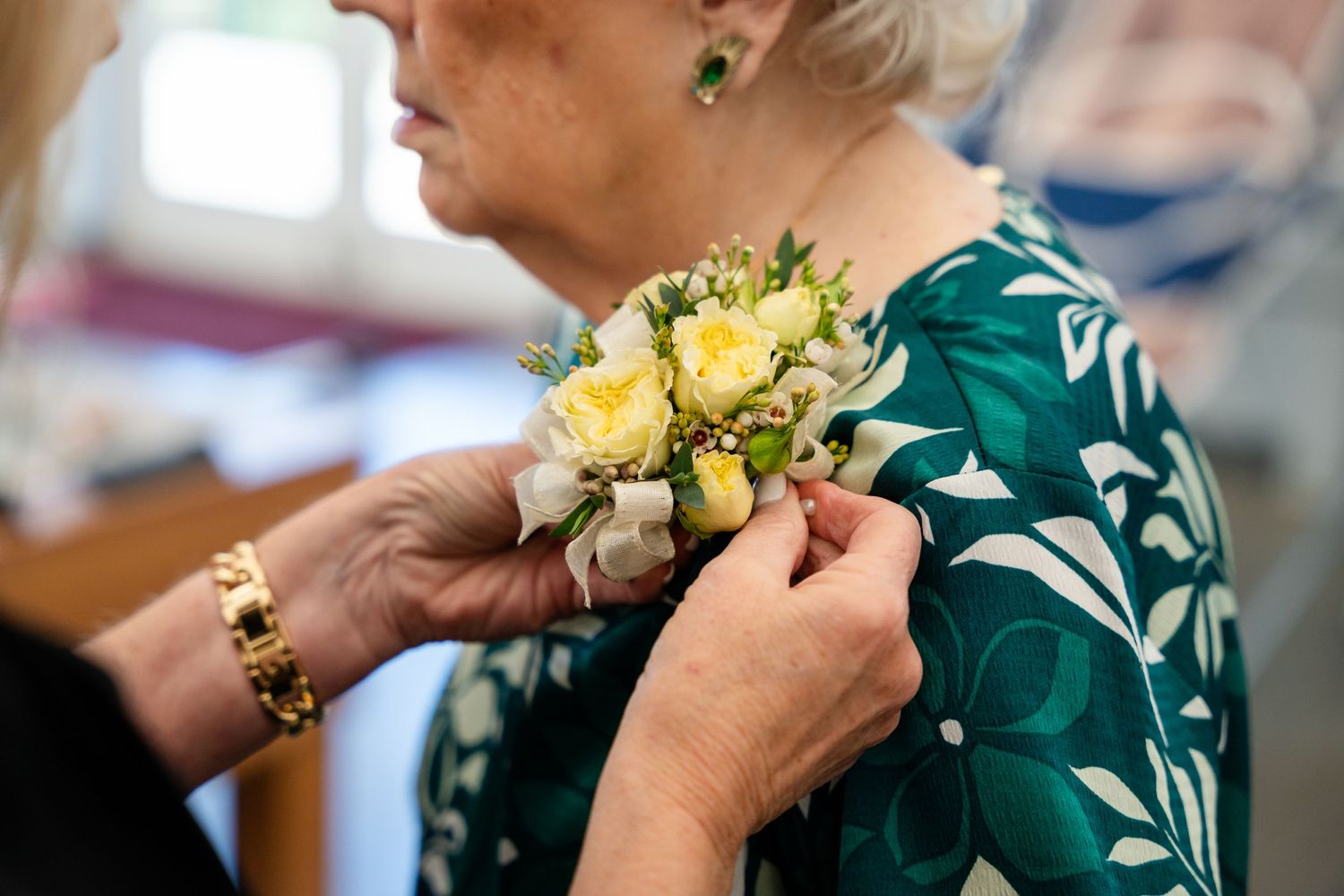 Someone pinning a yellow flower corsage onto a green floral dress.