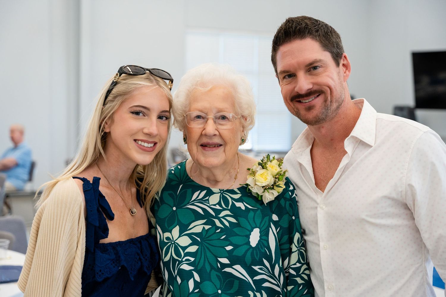 Three people pose together, with the center person wearing a green floral dress with yellow corsage.