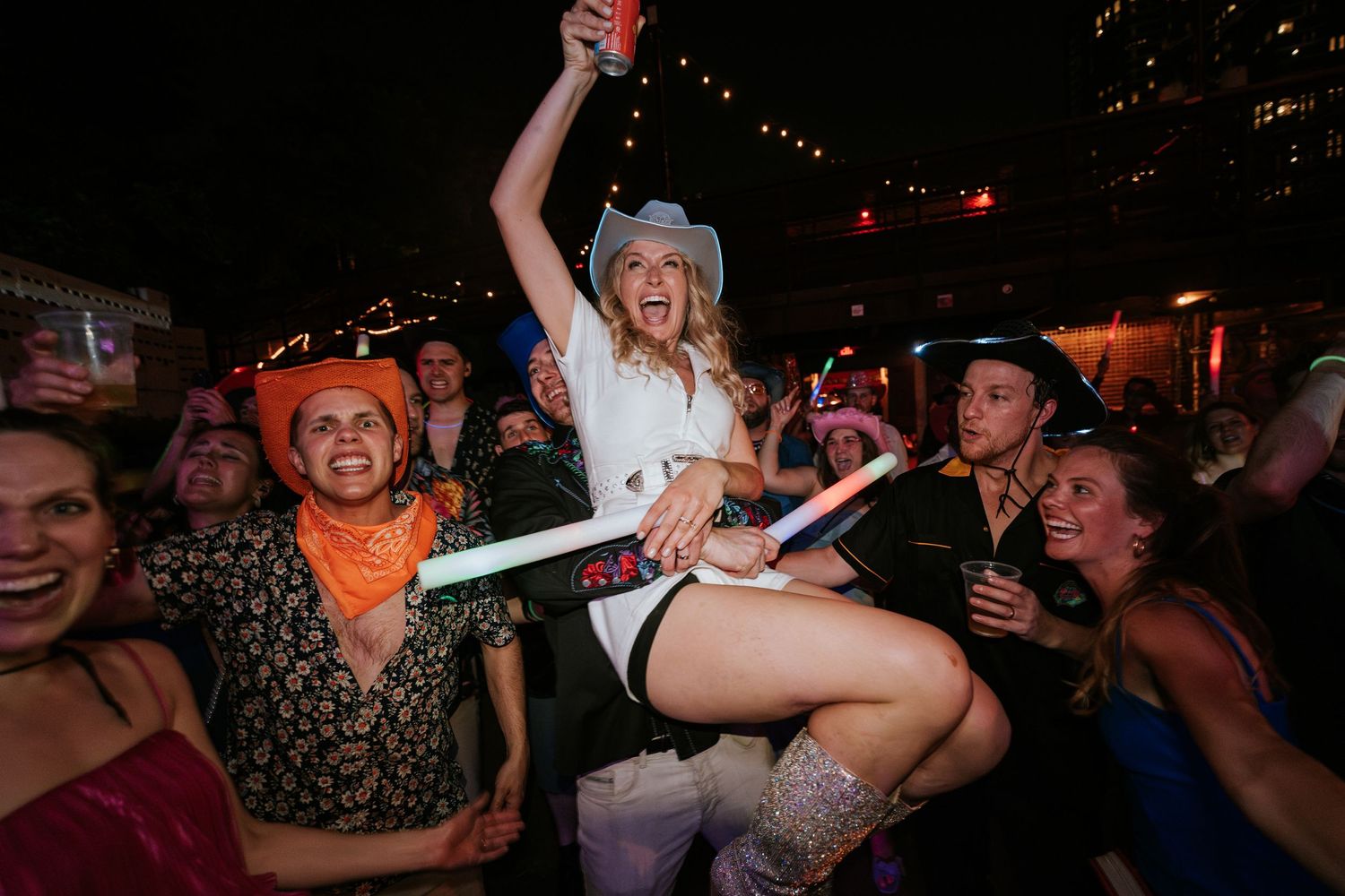 Energetic crowd celebrating with light-up sticks at nighttime party.