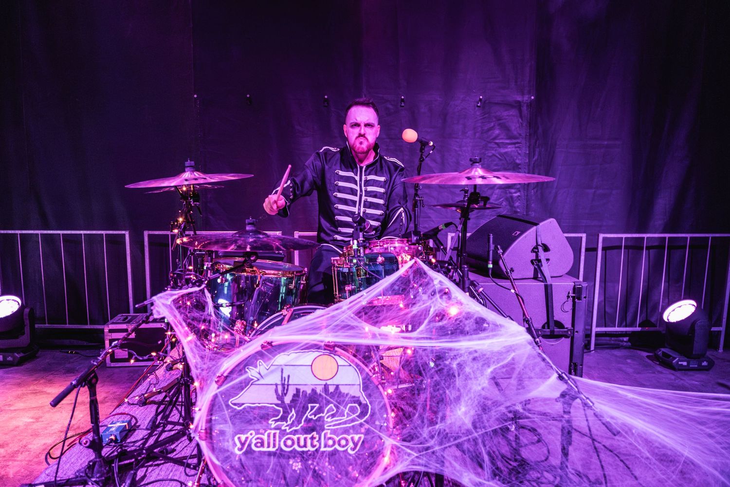 Drummer performing on stage with purple lighting and cobweb decorations on the drum kit.