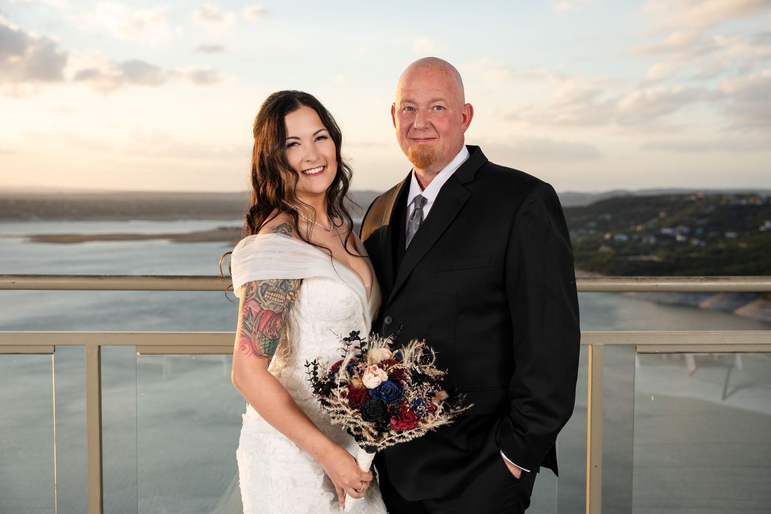 Wedding couple posing on balcony with coastal vista at sunset.