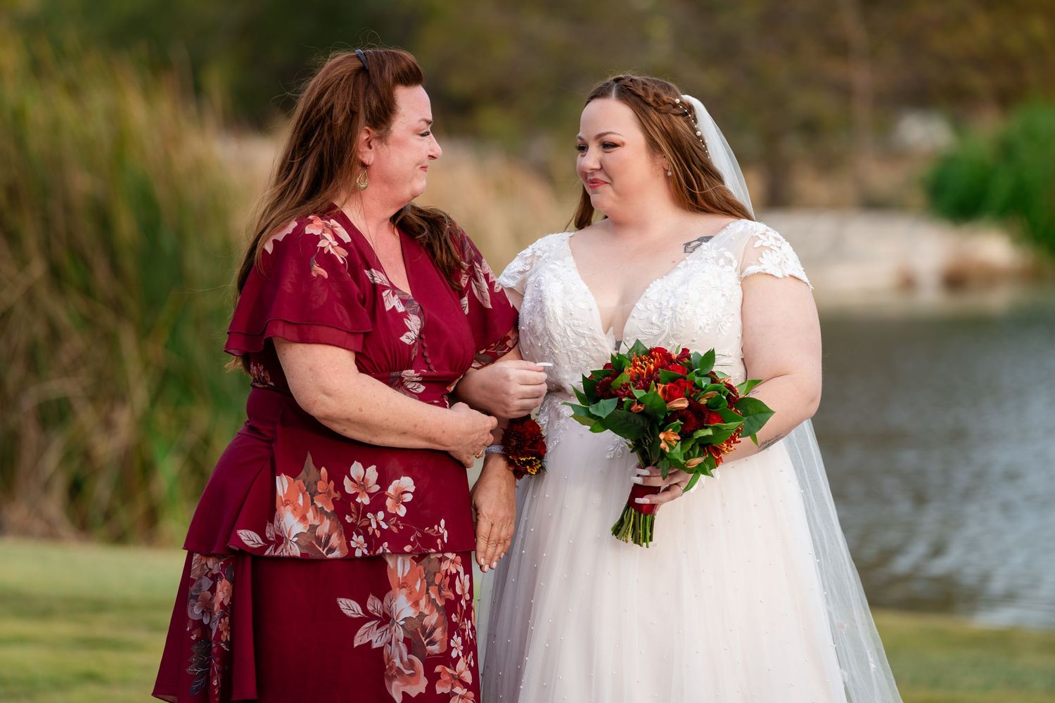 A touching moment between wedding party members by a lakeside setting with autumn scenery.