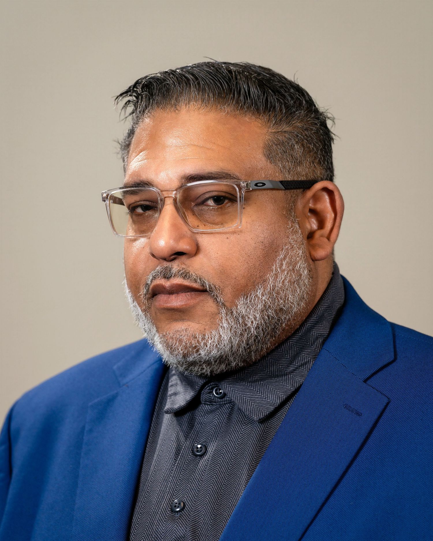 Professional headshot of a middle-aged man with glasses and a gray beard wearing a blue blazer.