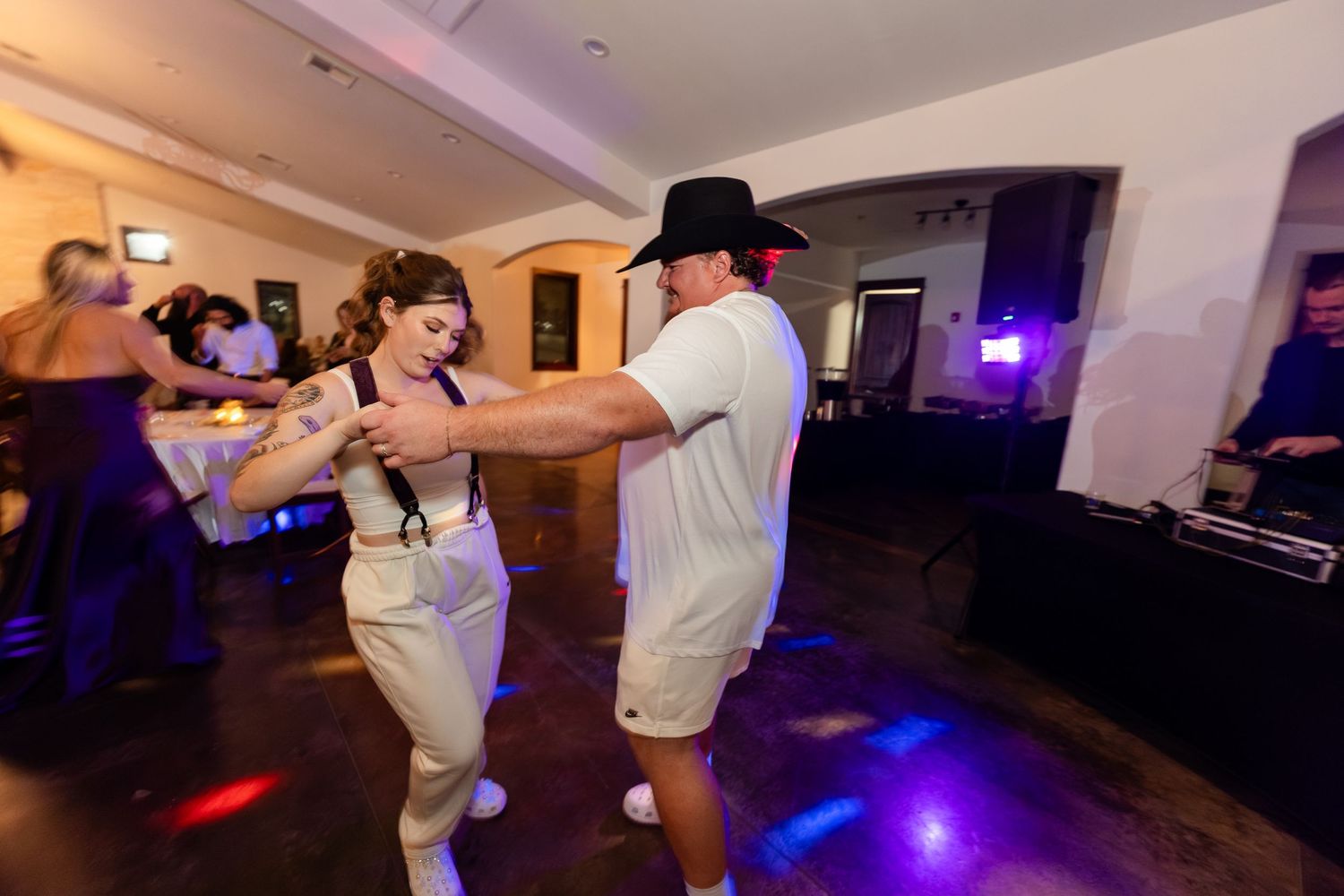 Couple dancing energetically on a colorful dance floor at a lively indoor party with DJ in background.