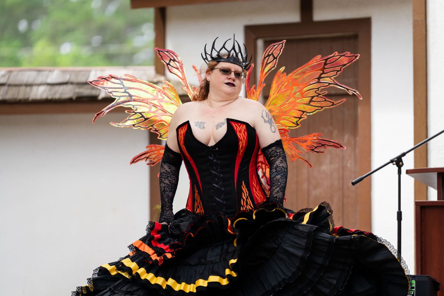 Woman in black red orange fairy costume with wings and corset performing outdoors at Renaissance faire.