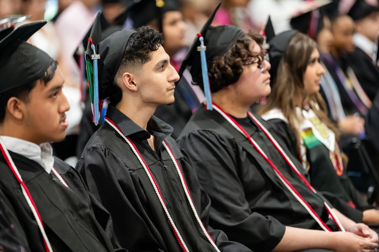 Students in black graduation gowns and caps seated at a commencement ceremony.