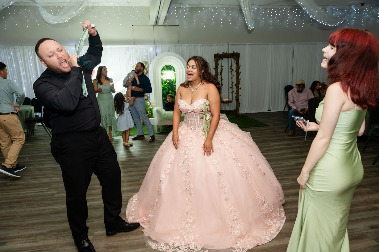 Young woman in pink ballgown dances with guests at a quinceañera celebration in a decorated event tent.