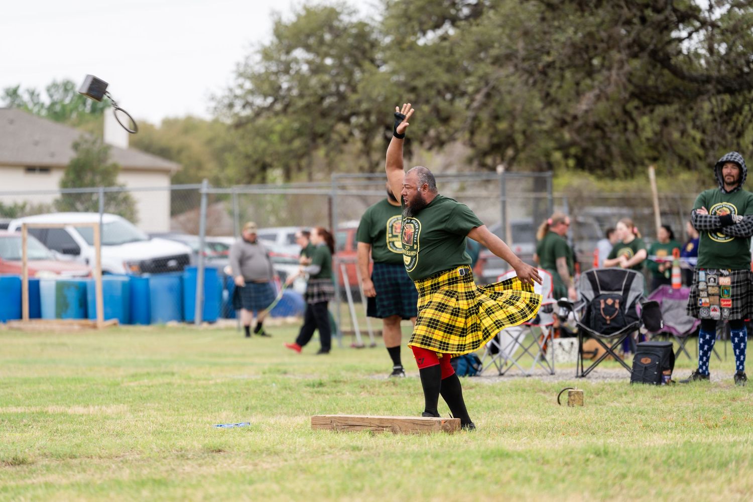 Man in tartan kilt performs Highland Games hammer throw at outdoor Scottish festival competition.